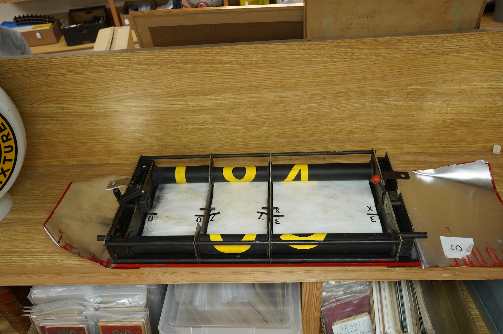 A London Transport bus destination blind box, complete with mechanism and three numerical destination blinds, with later applied sheets of red painted steel bolted to each side, mechanism with winding handle and row sele